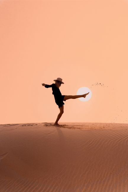 A person in silhouette kicks sand on a desert dune at sunset in Cape Town, South Africa.