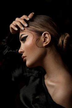 Profile portrait of an elegant woman with bold makeup and pearls on ear, posing gracefully in a studio setting.