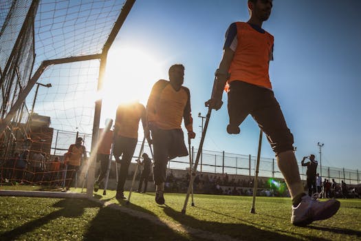 Amputee soccer players in orange jerseys competing on a sunny field.