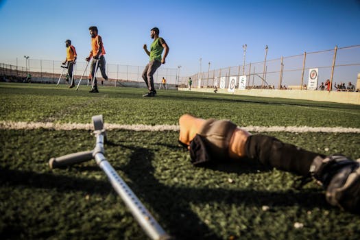 Amputee soccer players practice on a sunny field with crutches and prosthetic legs.