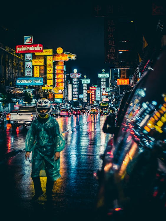 Homme En Imperméable Vert Et Casque Intégral Blanc Debout Au Milieu De La Rue Humide