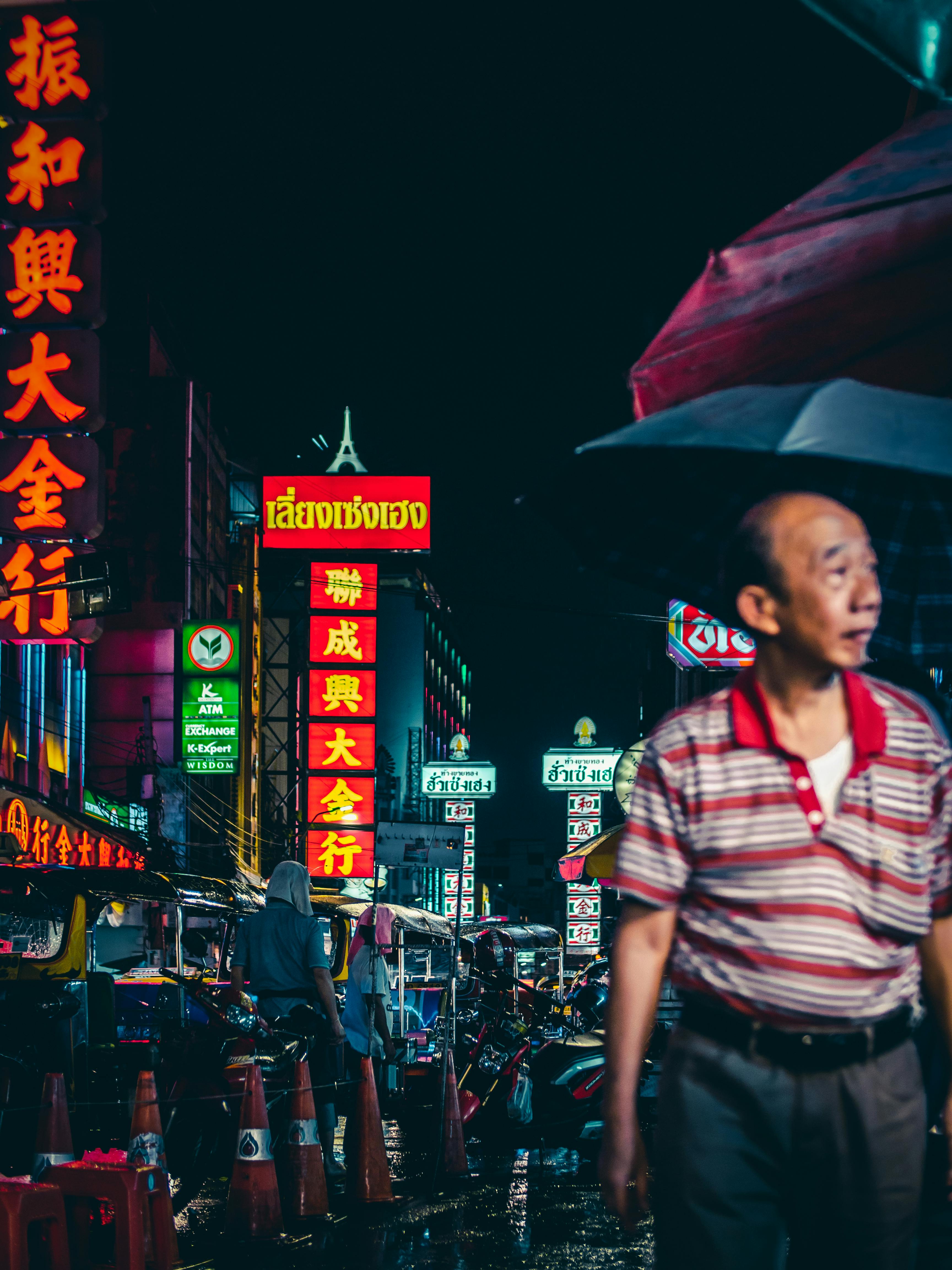 霓虹灯闪烁，雨夜中人们打着伞，城市一片热闹景象
