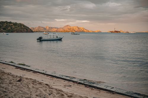 Free A tranquil beach view with boats on the water and mountains in the sunset light. Stock Photo