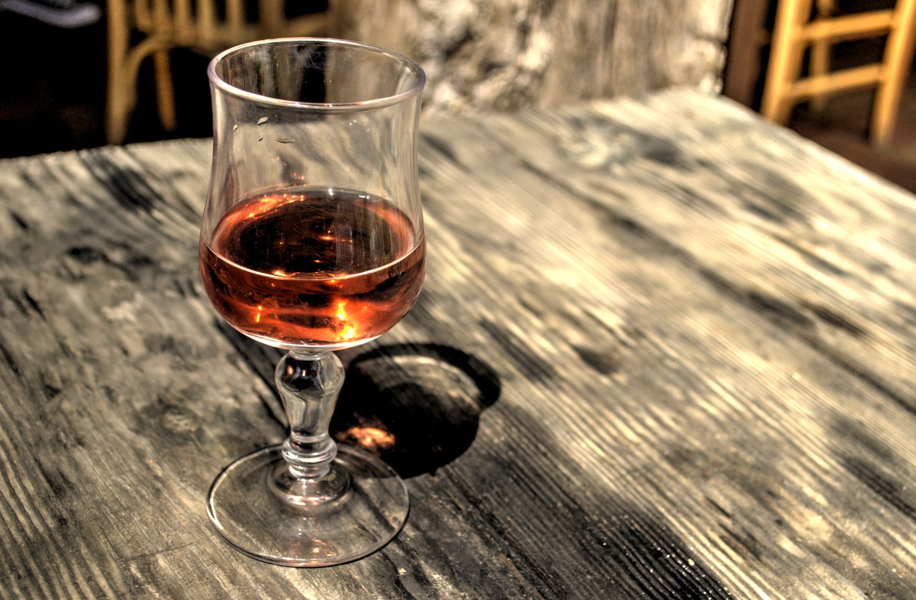 A glass of rose wine sits elegantly on a rustic wooden table, capturing a relaxed dining atmosphere.