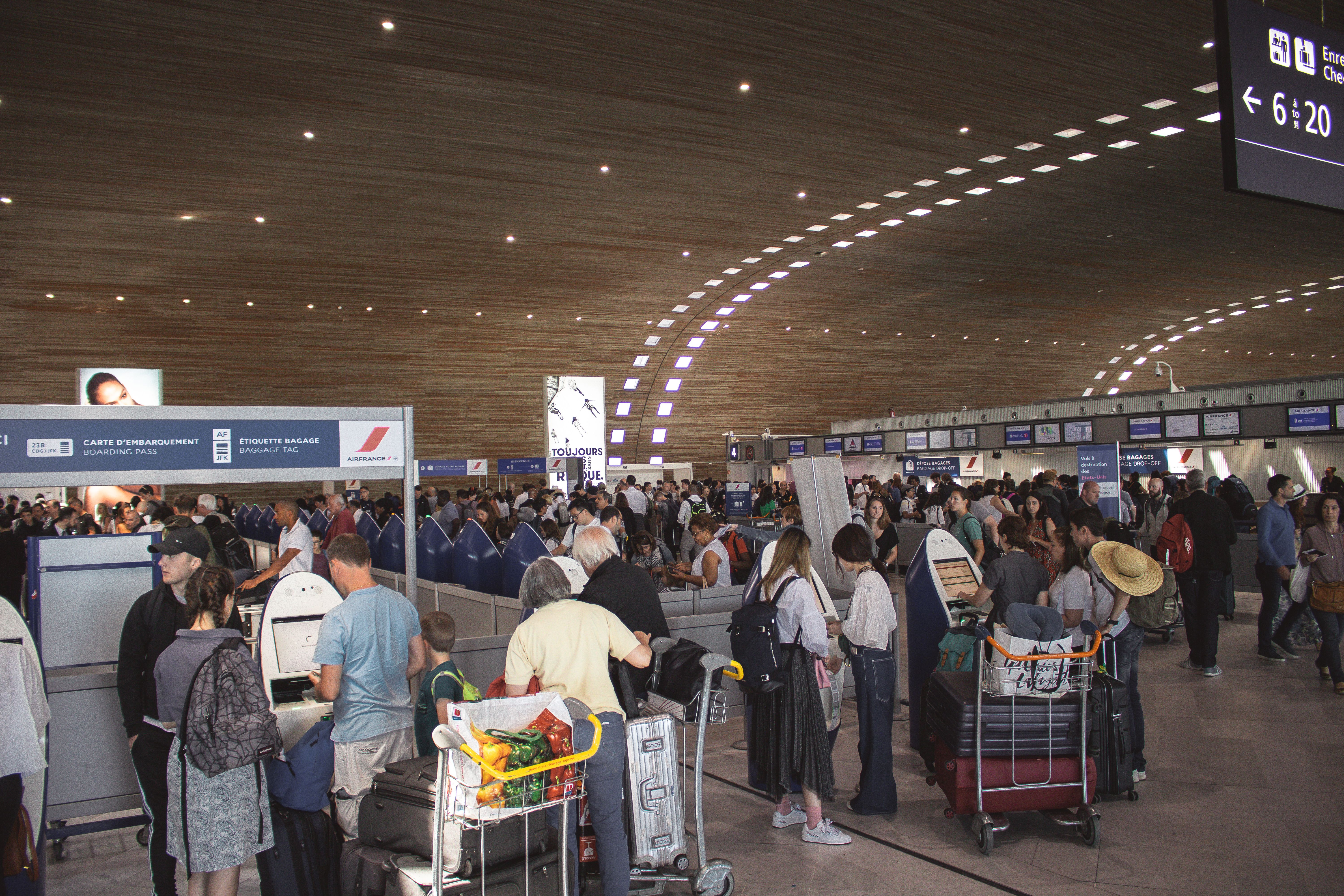 Travellers queue at airport check-in counters with luggage in a busy departure terminal