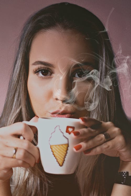Портретное фото женщины, дующей на дымящуюся керамическую чашку с горячим напитком