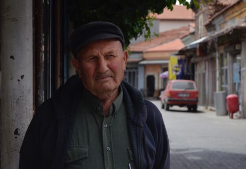 Free Portrait of an elderly man wearing a cap, standing on a quiet urban street. Stock Photo