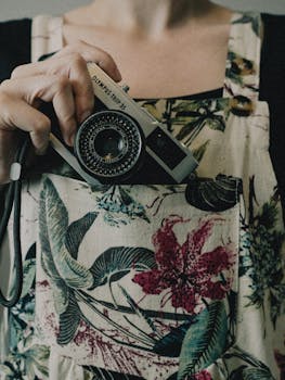 A woman holds a vintage camera against a floral patterned apron, showcasing retro photography style.