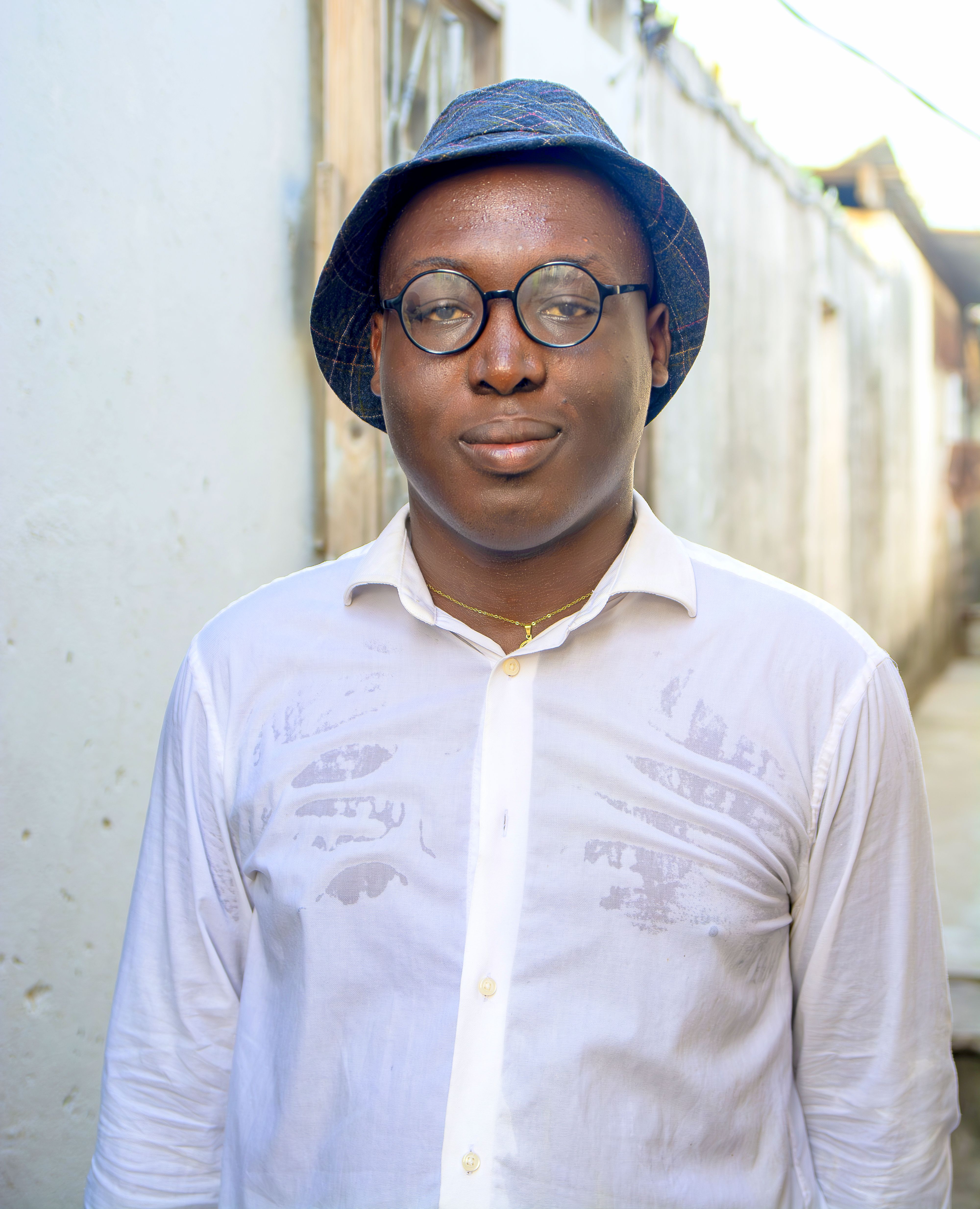 Outdoor portrait of a man wearing glasses and a hat in a narrow alleyway.