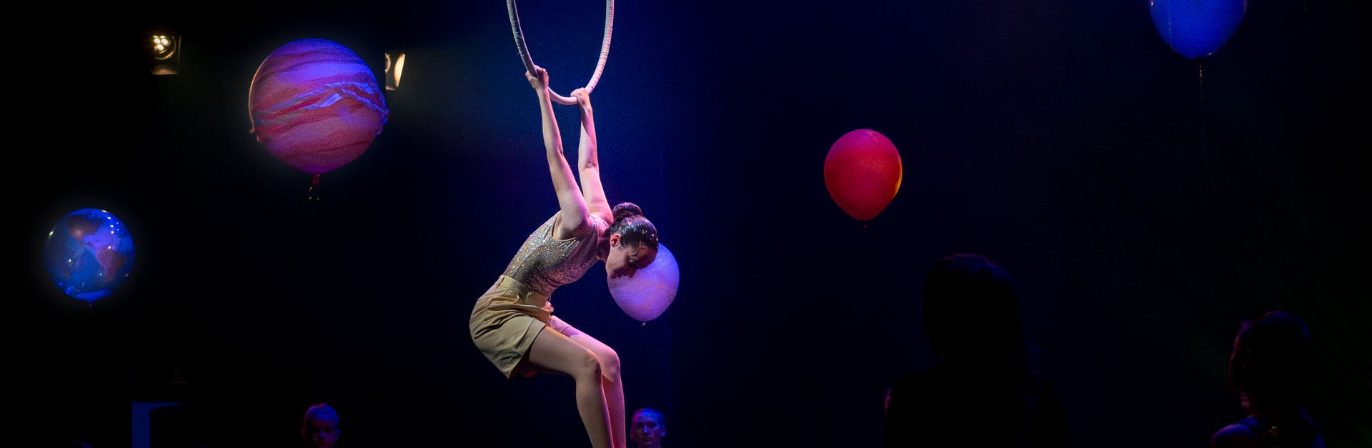 A captivating aerial acrobat performing in a ring amidst a stage decorated with planets.