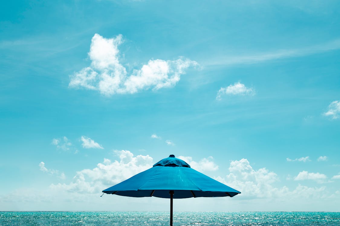 Close-up Photo of Blue Parasol Near Body of Water Under Blue Sky
