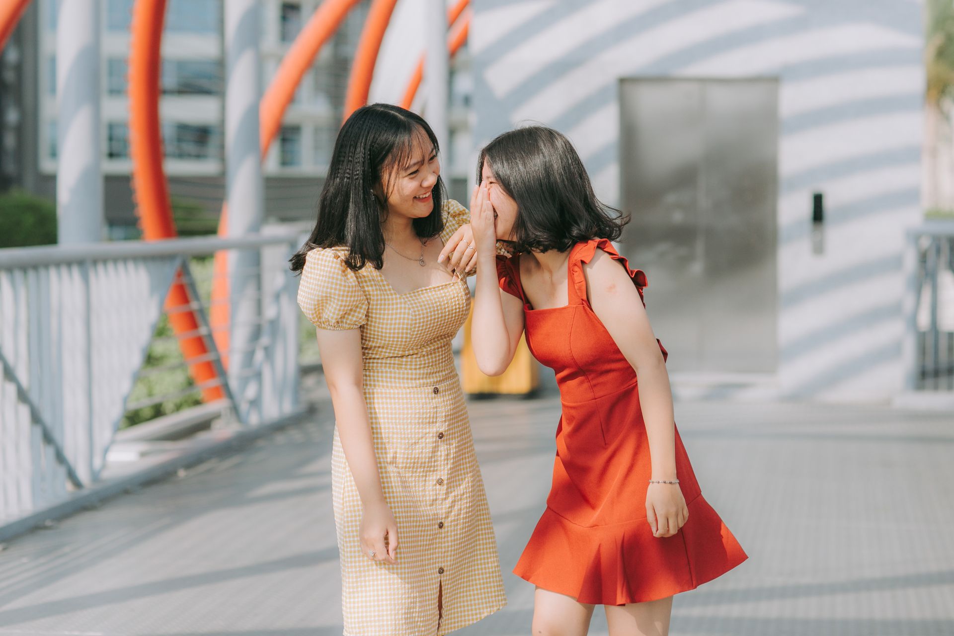 Two young women laughing and sharing a secret outdoors, exuding happiness and friendship.