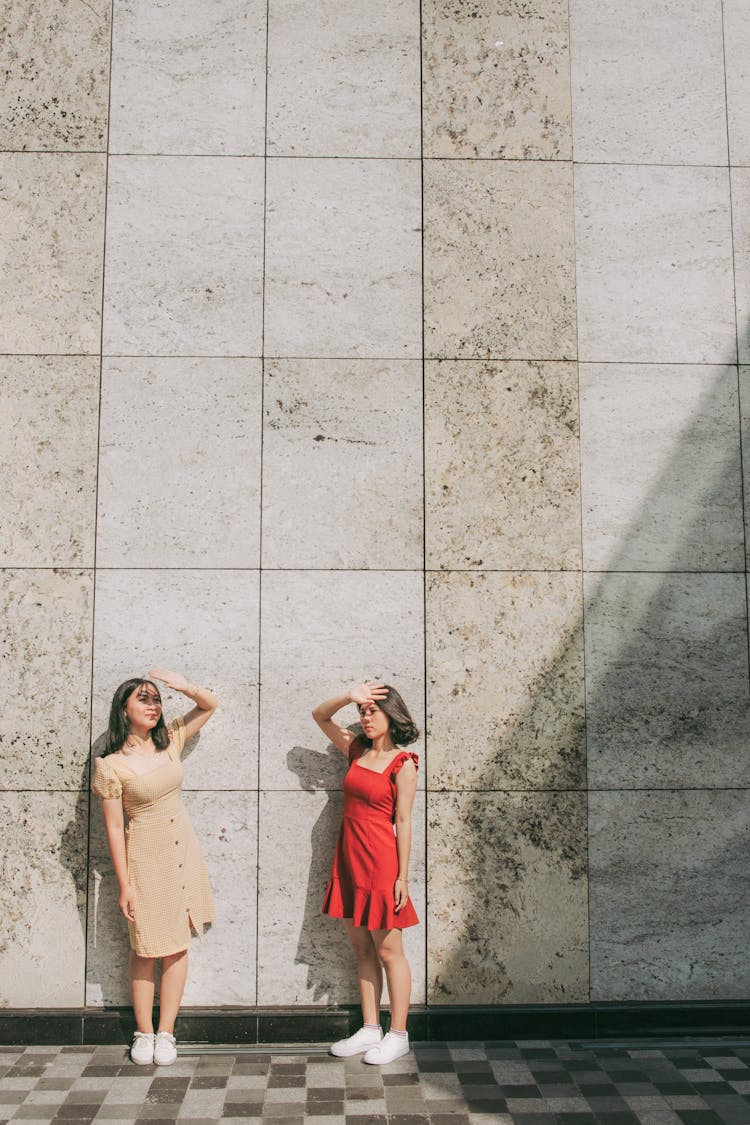 Photo Of Two Women Standing By Wall Posing While  Blocking Sun With Their Hands