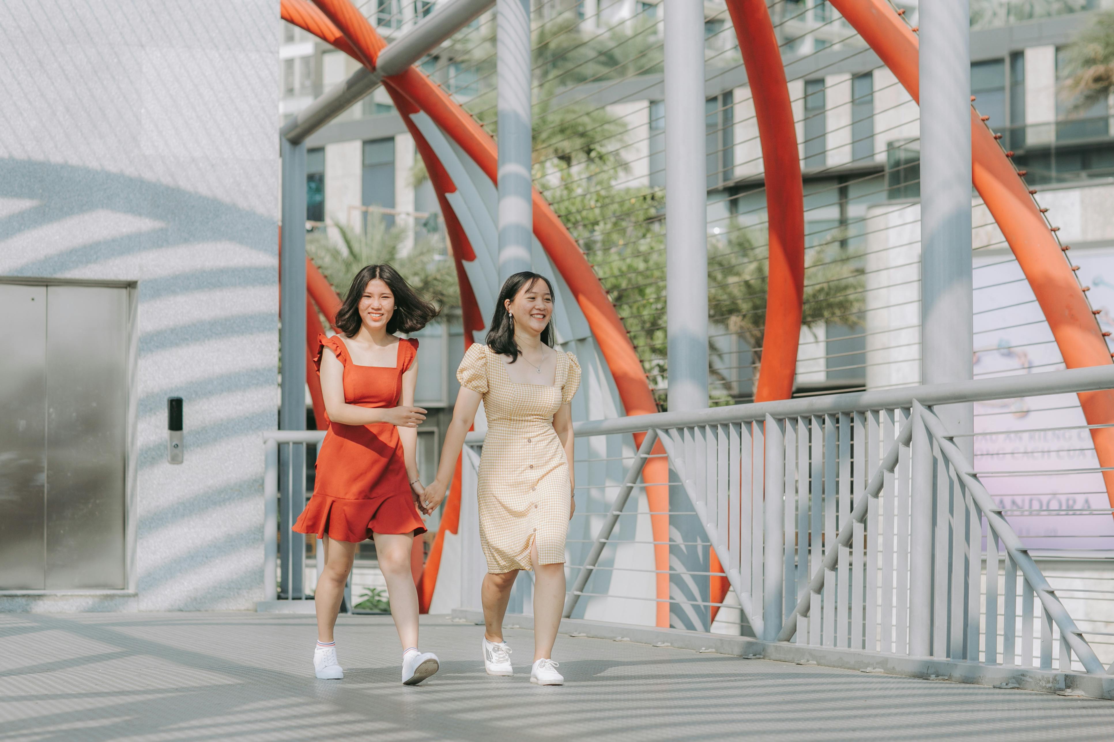 两个微笑的女人手牵着手，走在一座充满活力的现代桥上