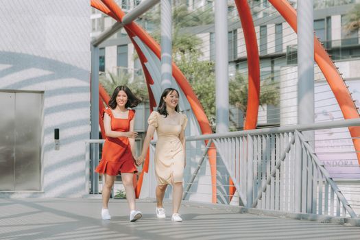两个微笑的女人手牵着手，走在一座充满活力的现代桥上