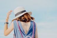 一个穿着蓝色衣服、戴着太阳帽的女人，背上有纹身，站在户外