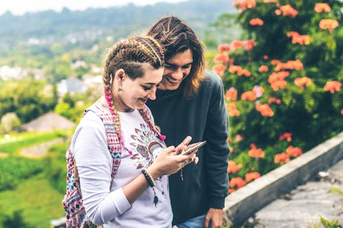 Photo of Man and Woman Smiling Looking at Mobile Phone