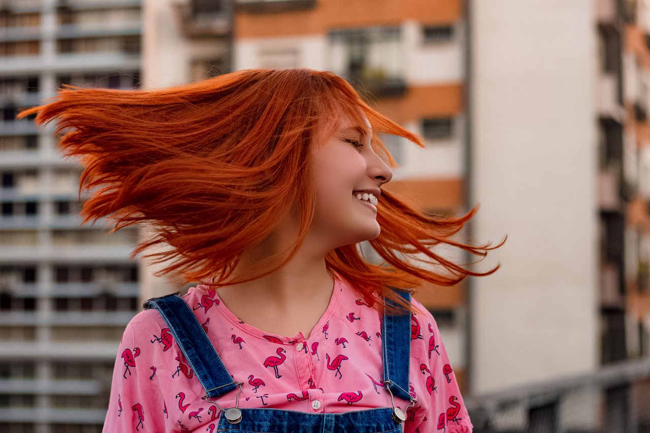 cheerful woman with vibrant red hair smiling outdoors in urban setting