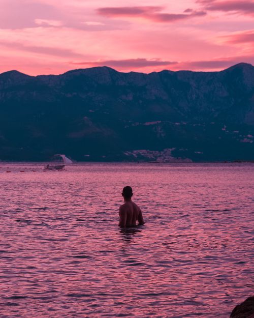 Free A lone figure in Montenegro's scenic lake at sunset, silhouetted against vibrant twilight hues. Stock Photo