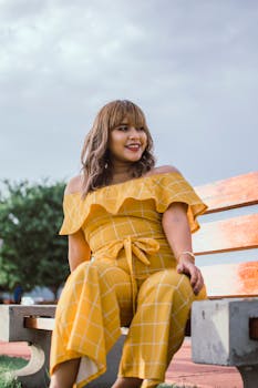 一位开朗的女子穿着黄色连身裤，坐在户外的木凳上