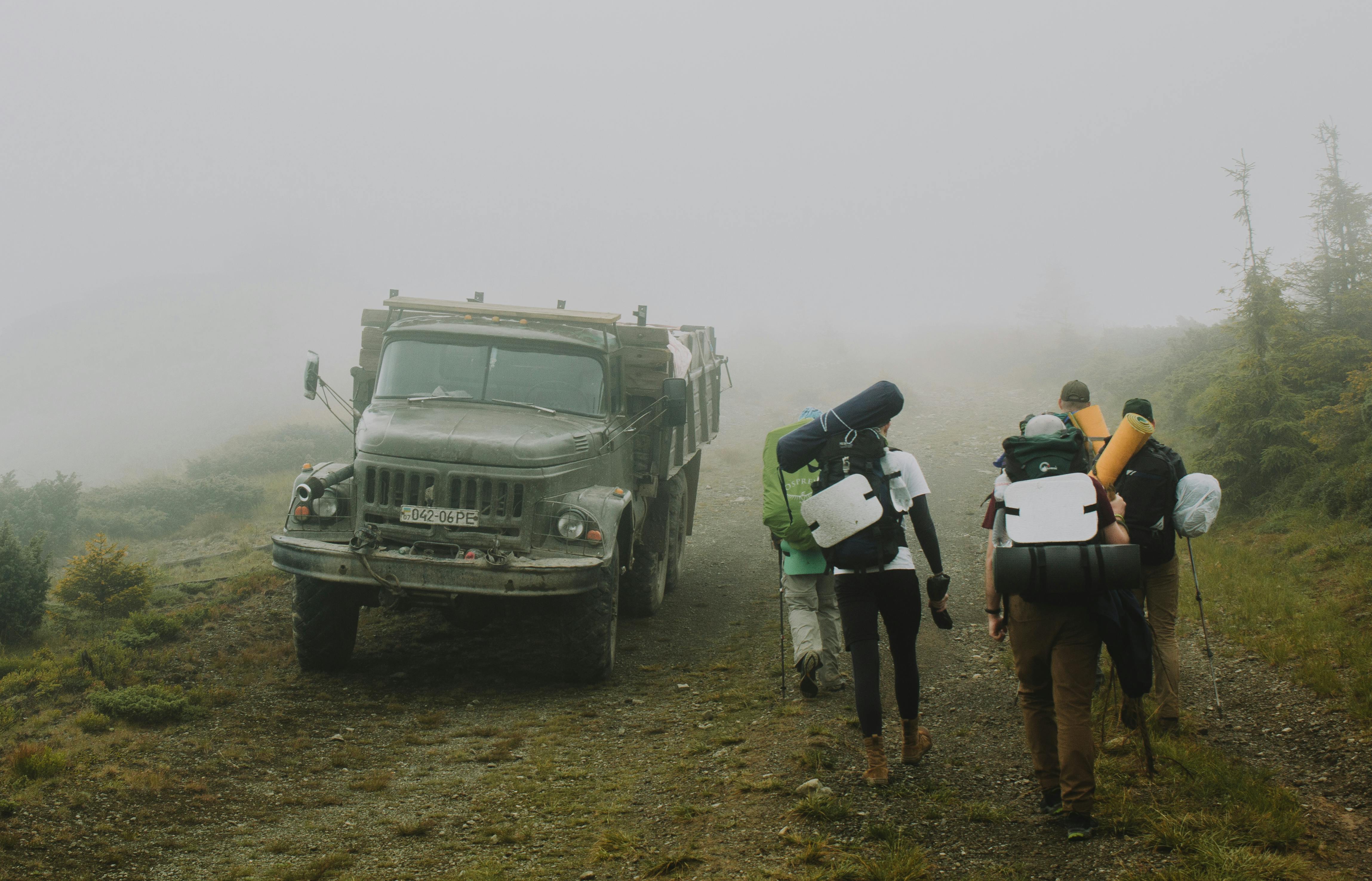 Hikers trekking on a misty path in the Carpathians, Ukraine, alongside an old truck.