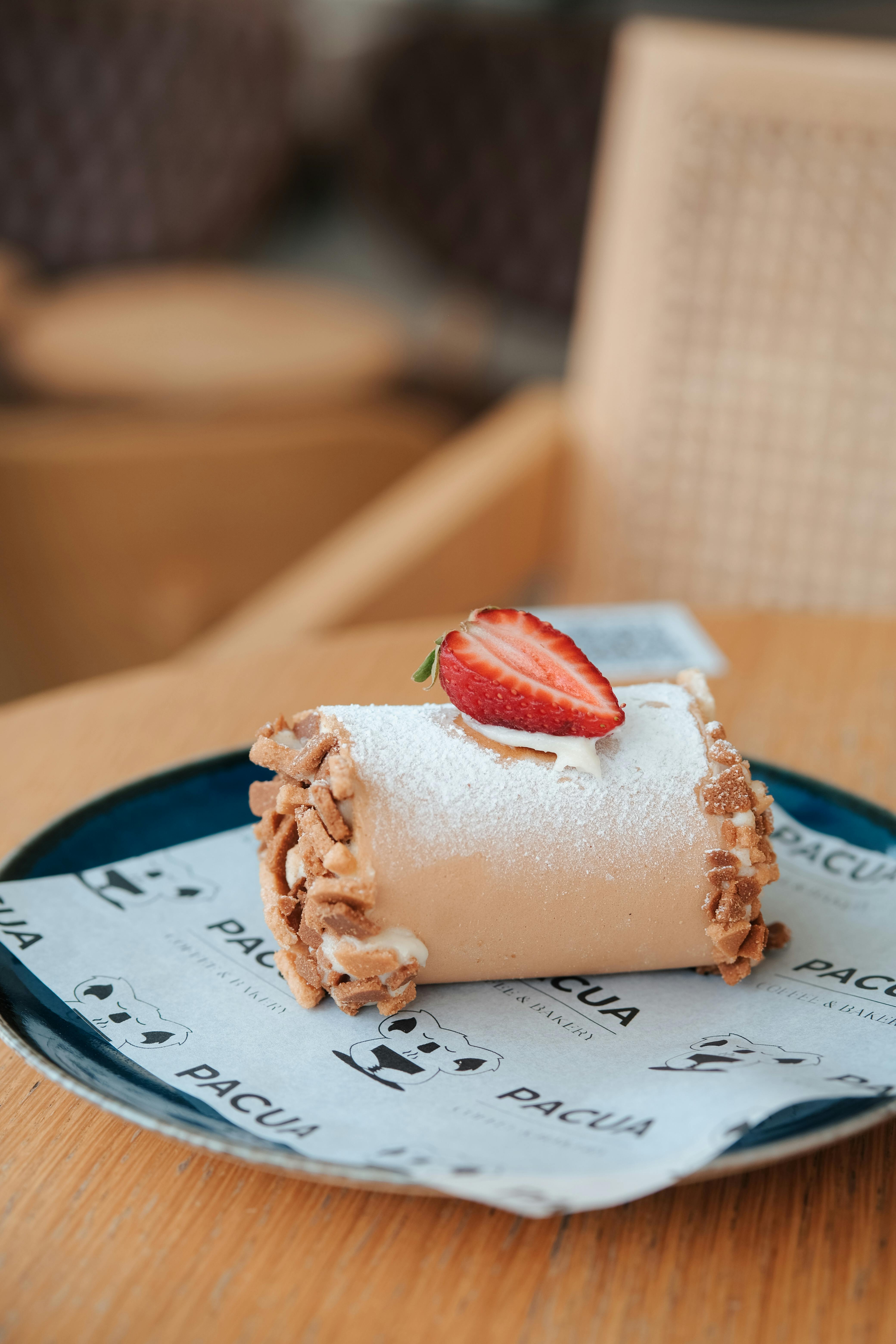 Close-up of a dessert roll with a strawberry garnish on a plate, showcasing intricate textures and sweet flavors.