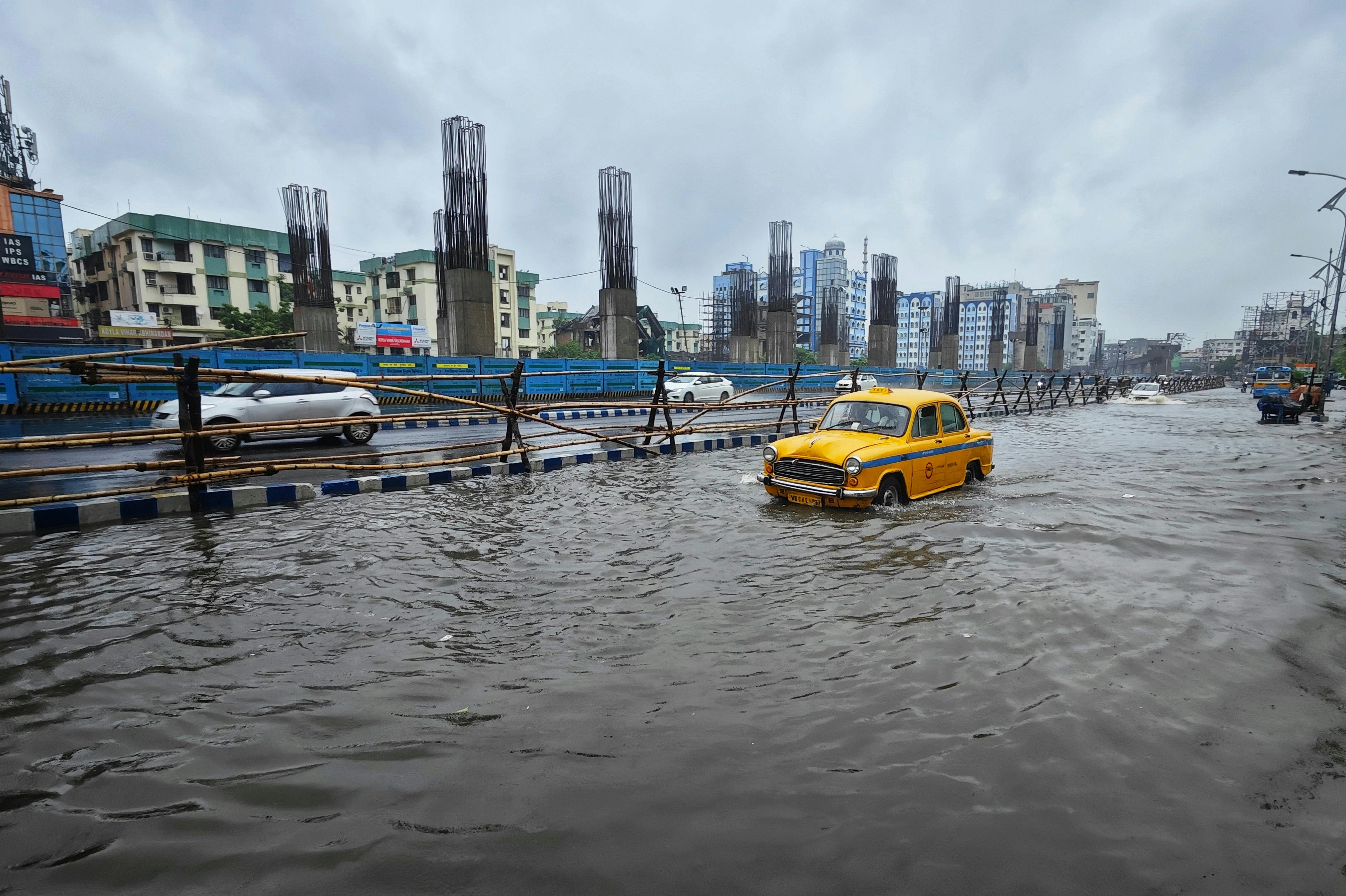 A flooded urban street in Kolkata with a classic yellow taxi navigating through the waterlogged road.