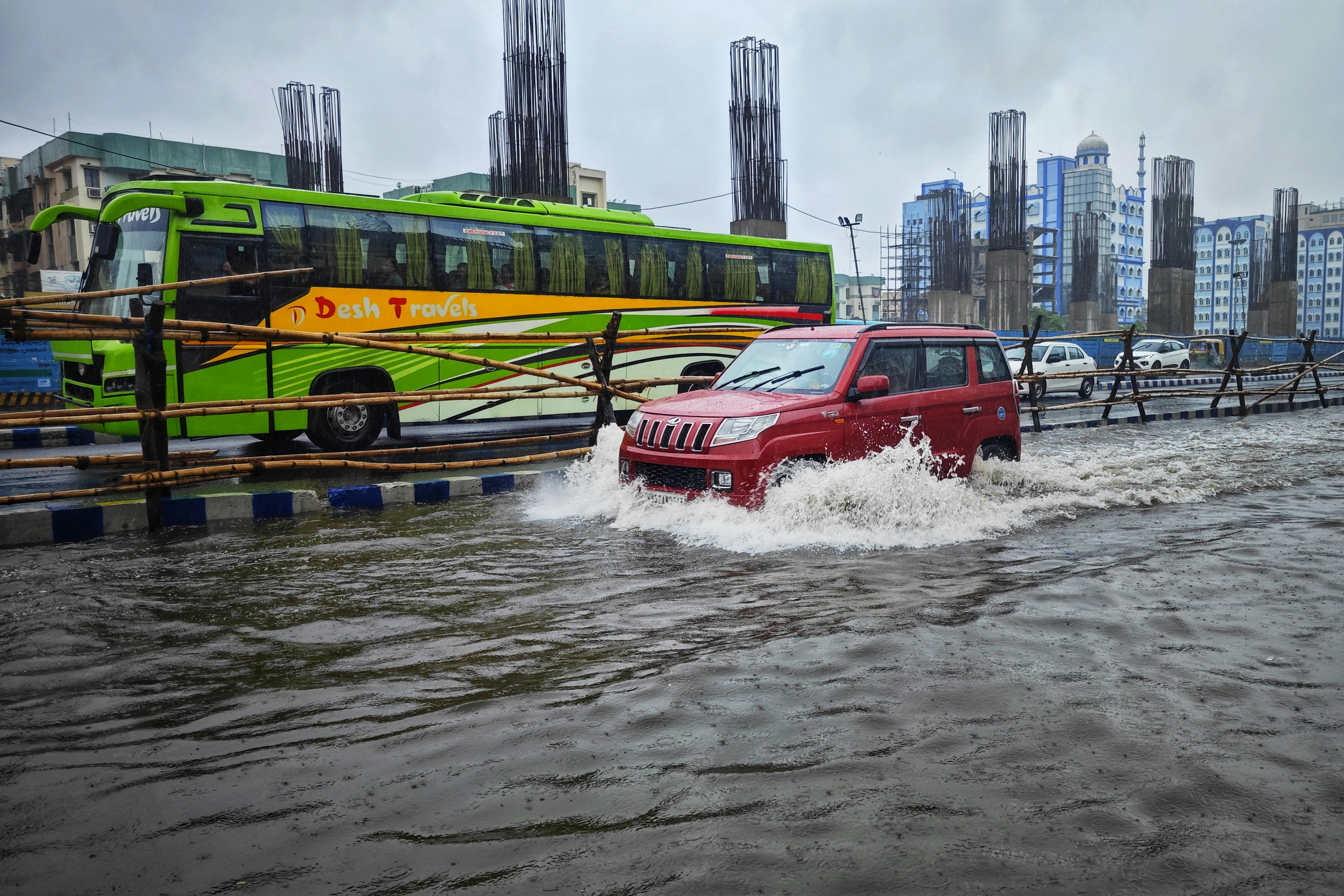 A red car and green bus navigate waterlogged streets in Kolkata after monsoon floods.
