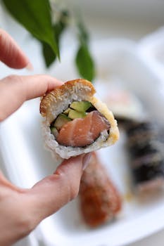 A hand holding a fresh salmon sushi roll with cucumber and rice, showcasing vibrant colors.