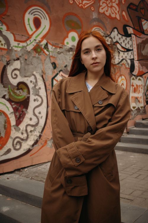 Free Model in a stylish coat stands confidently by vibrant street art in Tomsk, Russia. Stock Photo