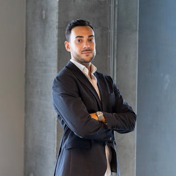 A poised businessman in formal attire standing confidently indoors with arms crossed.