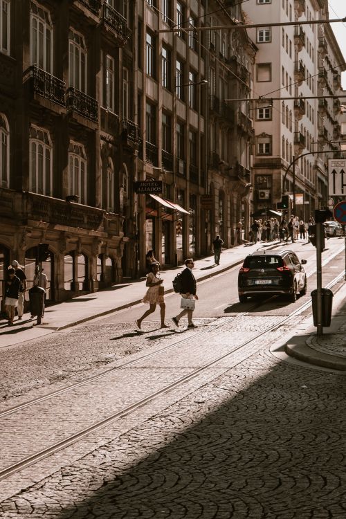 Free People cross a cobblestone street in historic Porto, Portugal during the day. Stock Photo