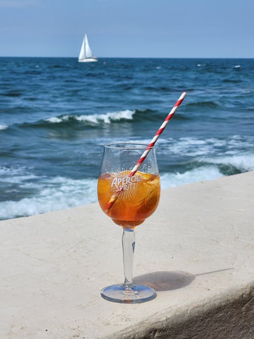 A glass of wine with a straw and a sailboat in the background