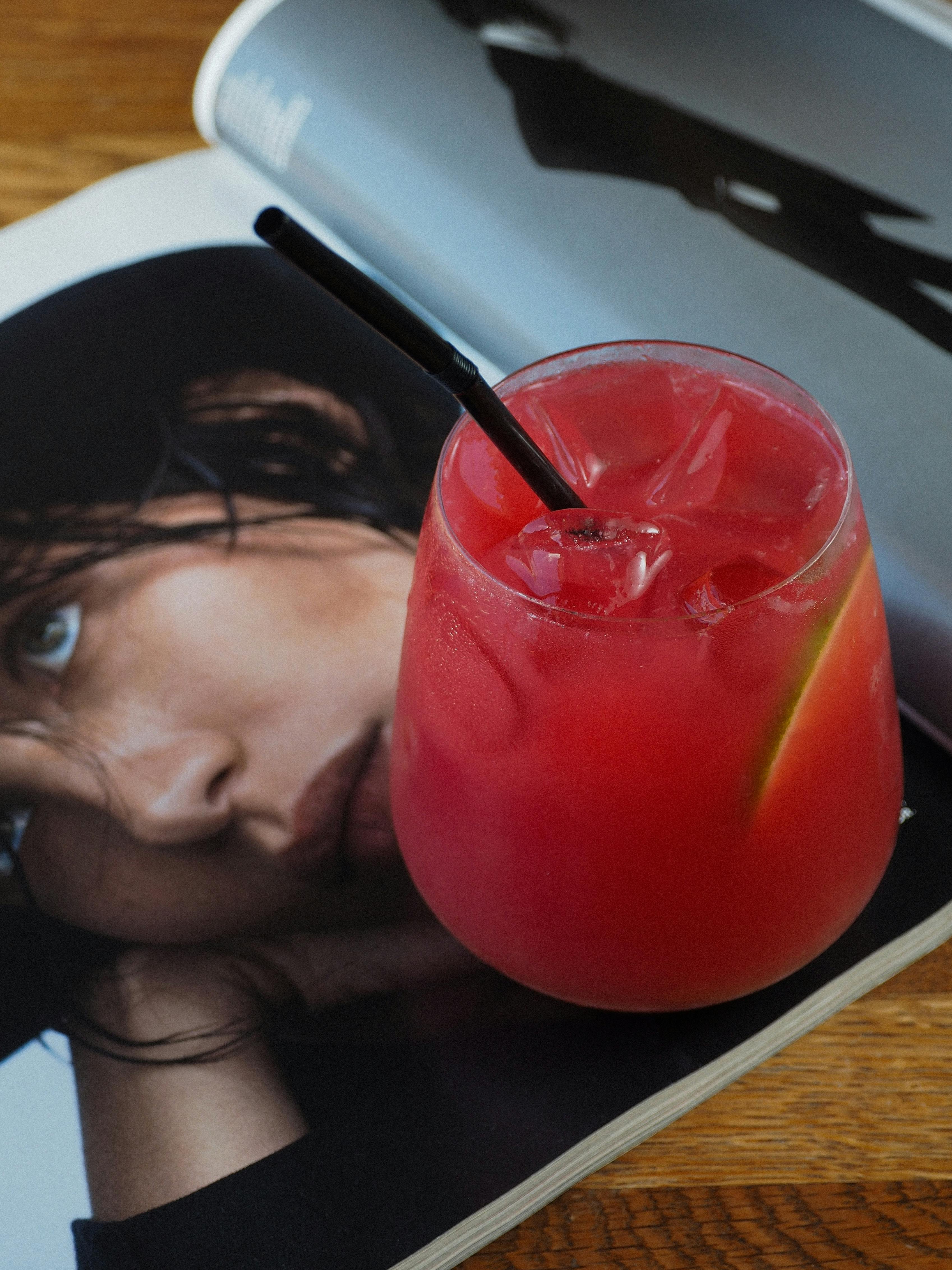 A vibrant red cocktail with a straw sits on a glossy fashion magazine.