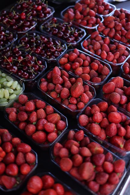 A vibrant display of organic strawberries, cherries, and grapes in plastic containers at a market.