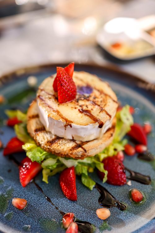 Free Delicious gourmet salad topped with grilled goat cheese, strawberries, and balsamic glaze on a blue plate. Stock Photo