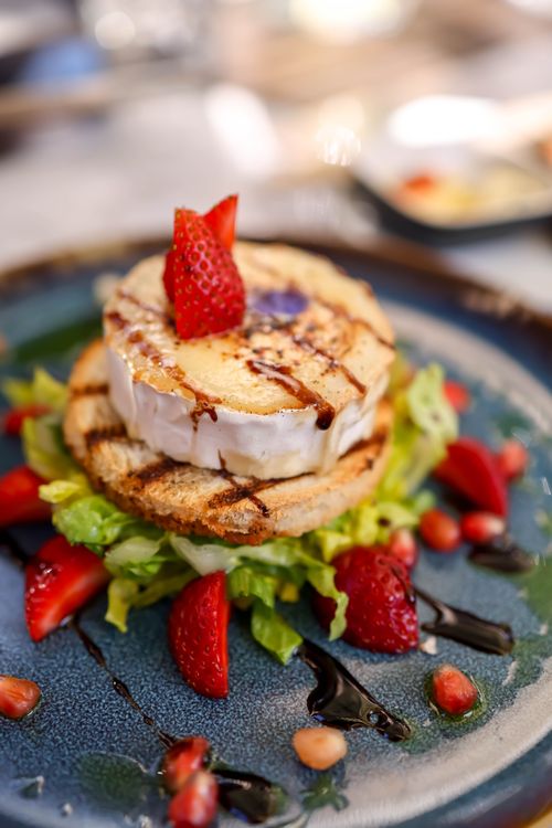 Free Elegant gourmet plate with camembert cheese, strawberries, and lettuce on a blue dish. Stock Photo
