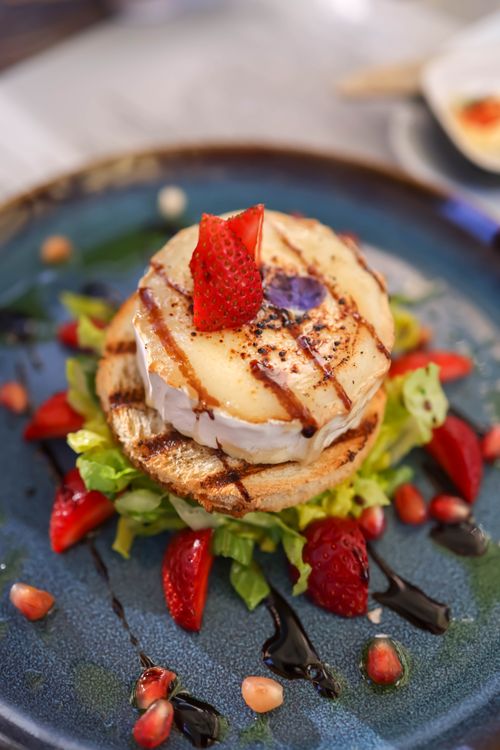 Free Elegant gourmet salad featuring goat cheese, strawberries, and balsamic glaze on a blue plate. Stock Photo