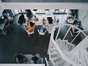 从俯视角度看现代工作空间，桌子周围有人和螺旋楼梯