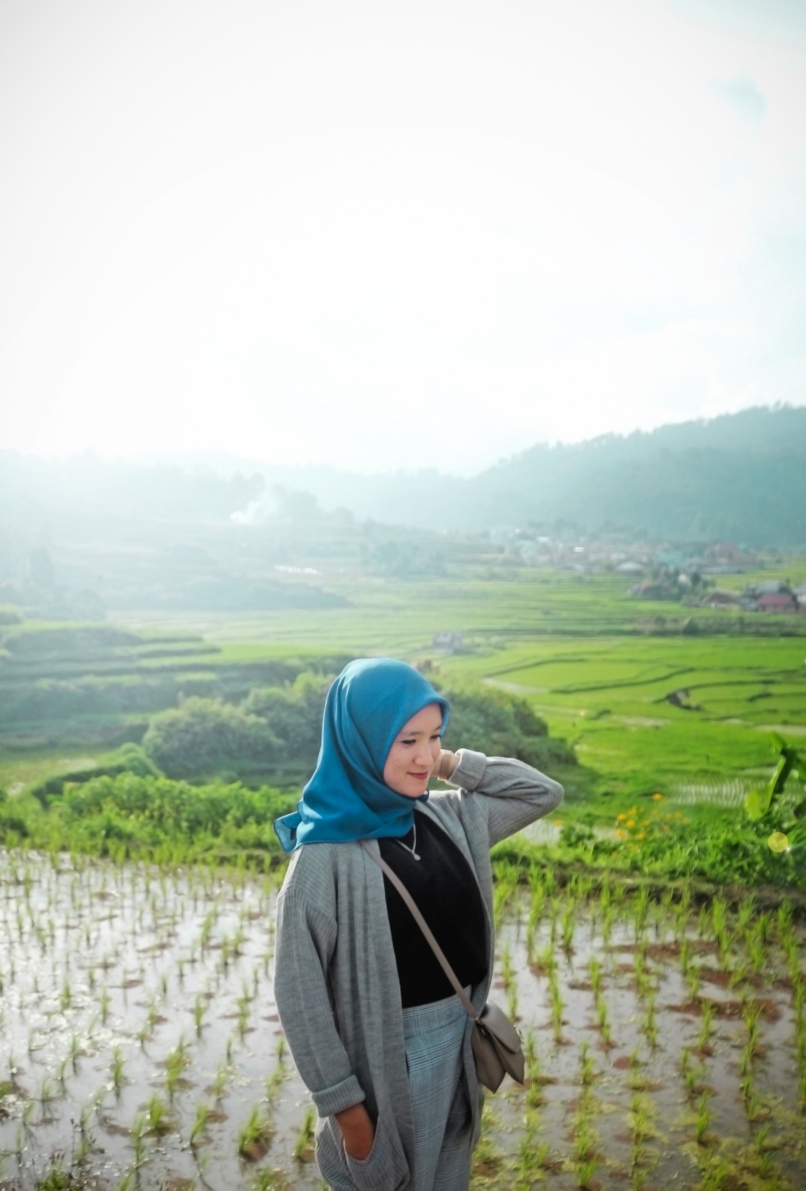Content Muslim female wearing headscarf and smiling away on background of green plantations in sunlight
