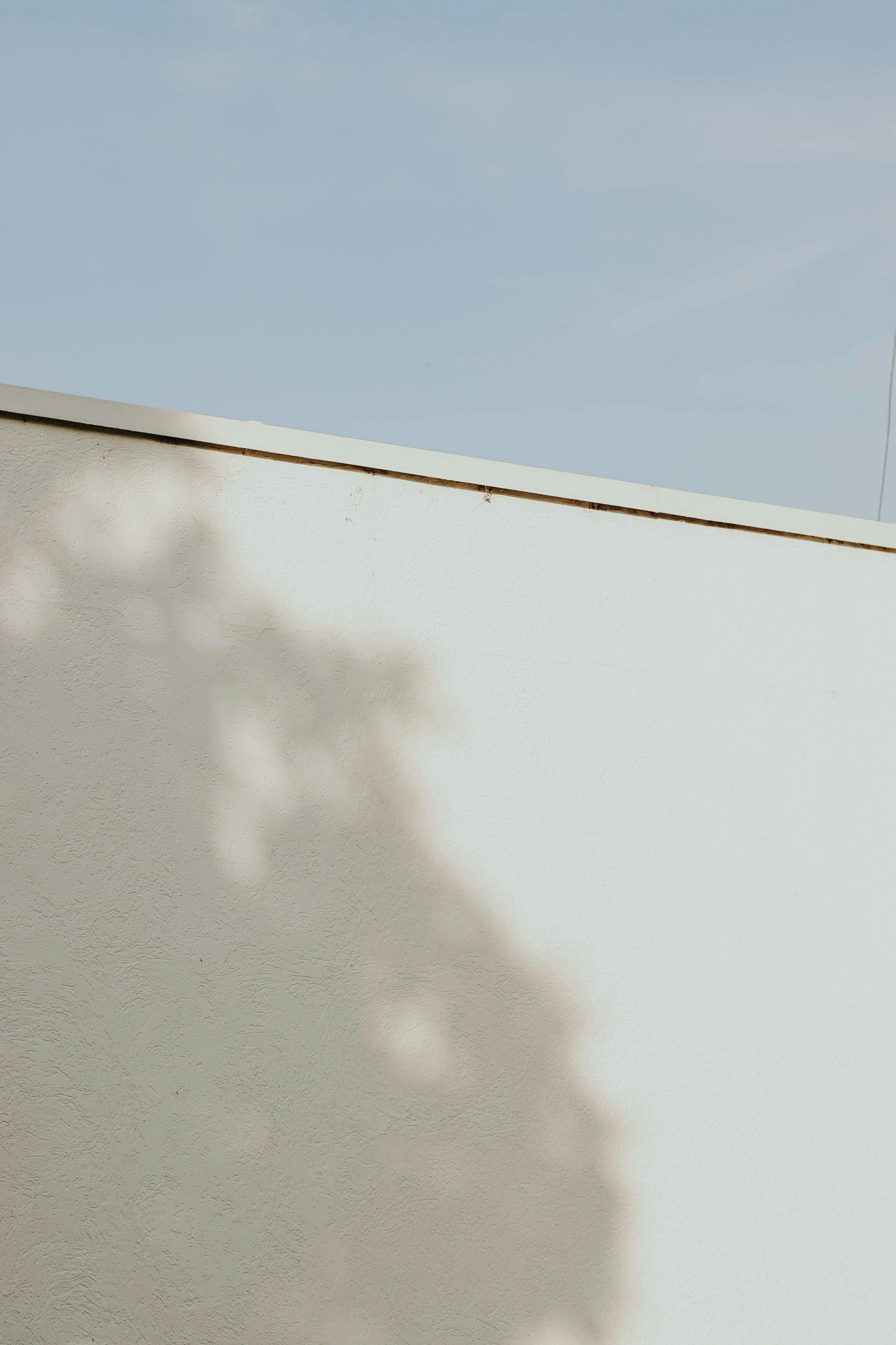 Shadow pattern on a white wall with a clear blue sky creates a minimalist aesthetic.