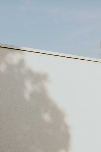 Shadow pattern on a white wall with a clear blue sky creates a minimalist aesthetic.