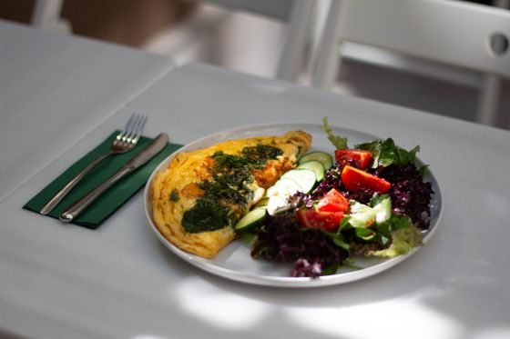 Folded omelette spread with basil pesto beside a salad of greens, cucumber and tomatoes