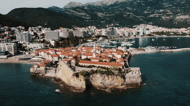 Drone capture of Budva Old Town with red roofs and Adriatic Sea, showcasing Montenegro's coastal beauty.