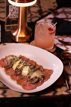Plated carpaccio paired with a crafted cocktail, capturing fine dining ambiance.