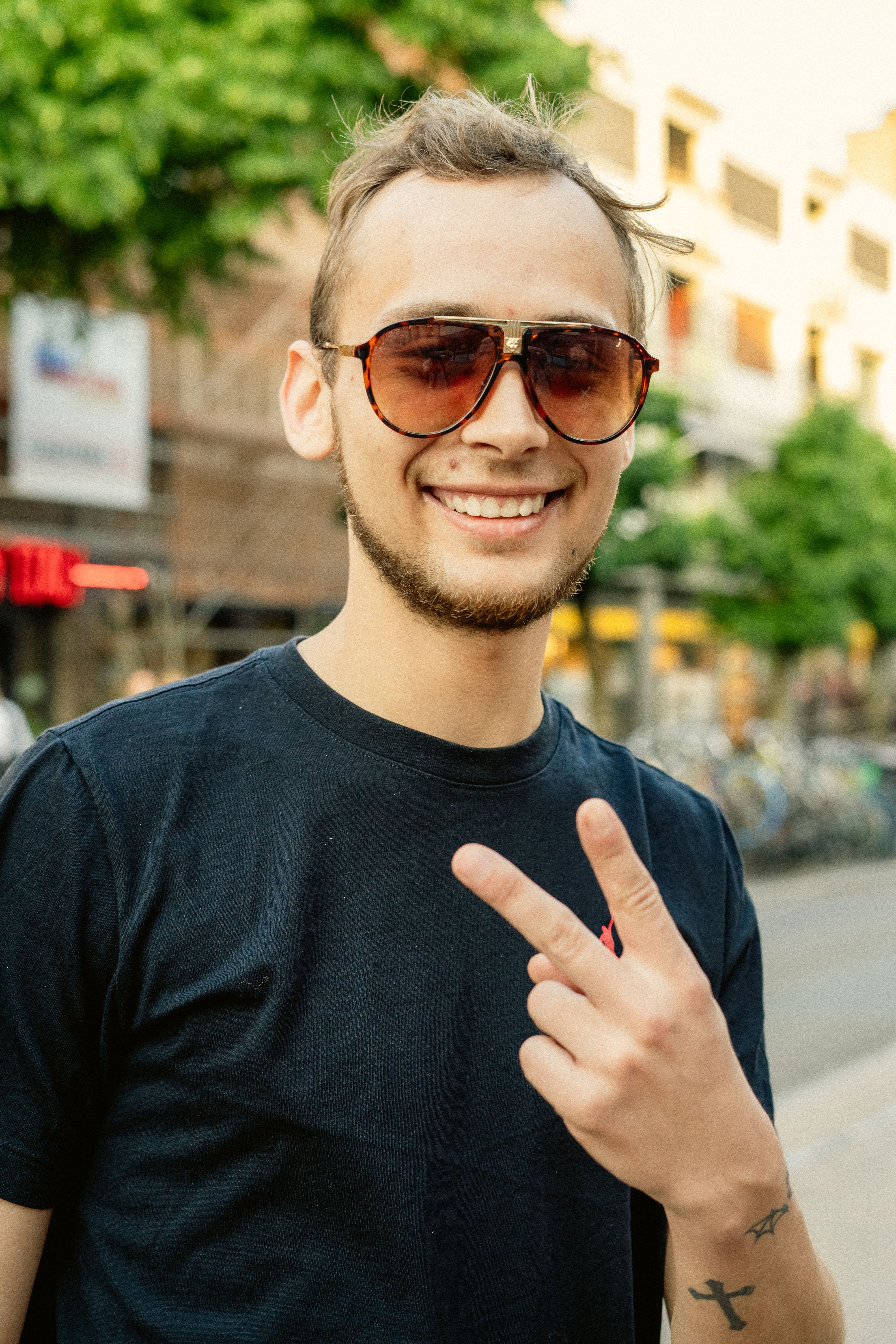 Young man wearing sunglasses and a black shirt making peace gesture on city street in Emden, Germany.