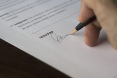 A hand signs a formal contract with a pen on a wooden desk.
