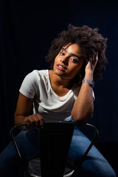 Portrait of a fashionable woman with curly hair sitting on a chair posing indoors.