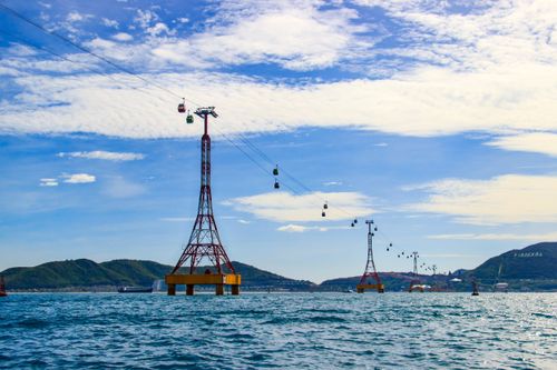 Free Cable cars traverse over a vibrant blue ocean with a clear sky, creating a picturesque coastal scene. Stock Photo