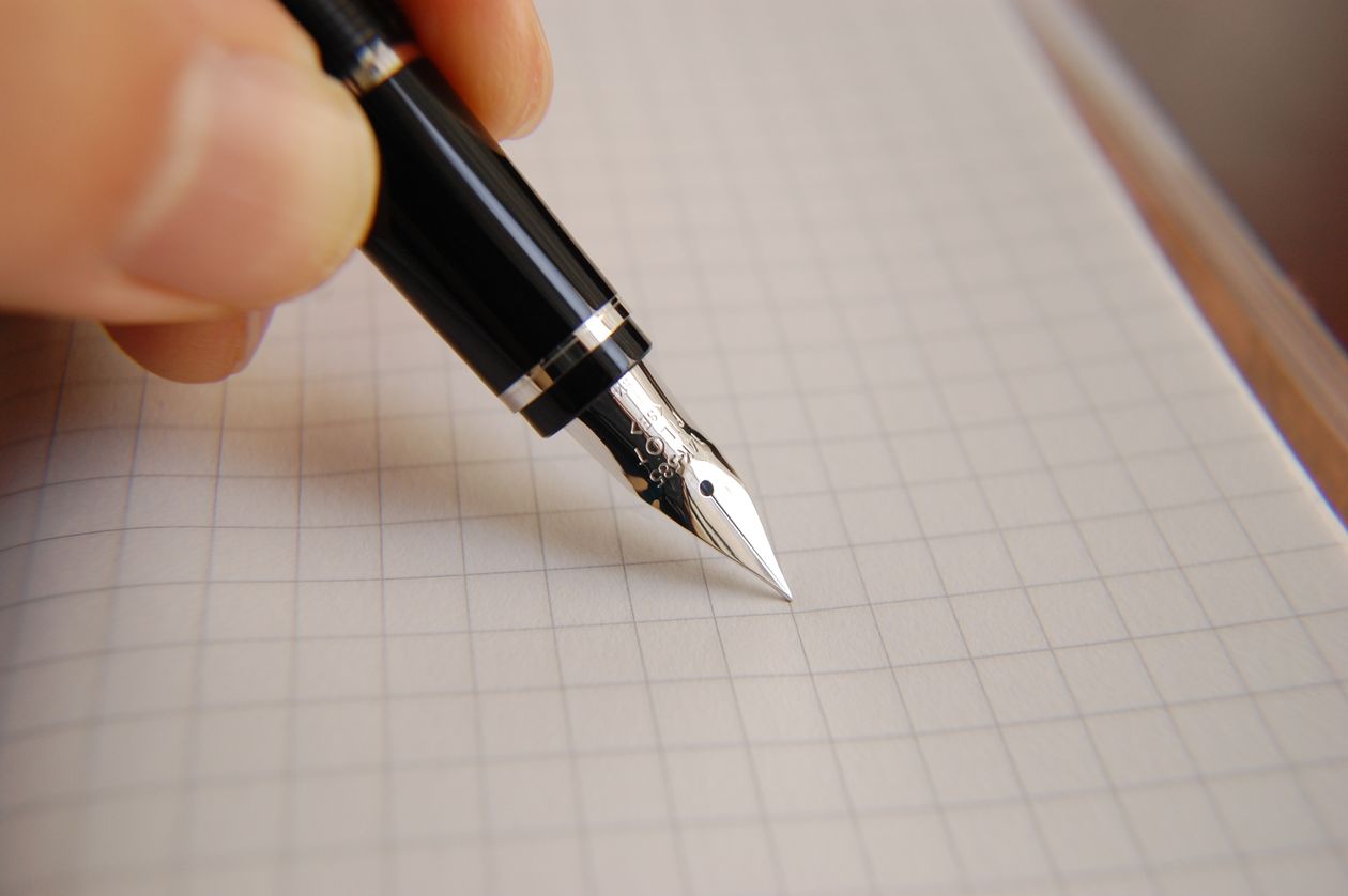 A detailed close-up of a black fountain pen poised over graph paper — fountain pen line quality
